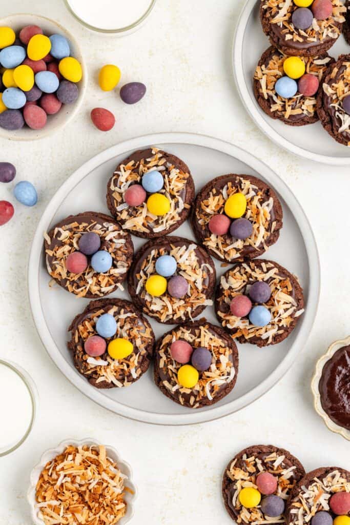 Cookies topped with coconut and candy eggs on a white plate; milk and additional treats nearby.