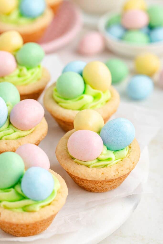 Mini Easter cookie cups with green frosting, topped with pastel-colored candy eggs on a white surface.