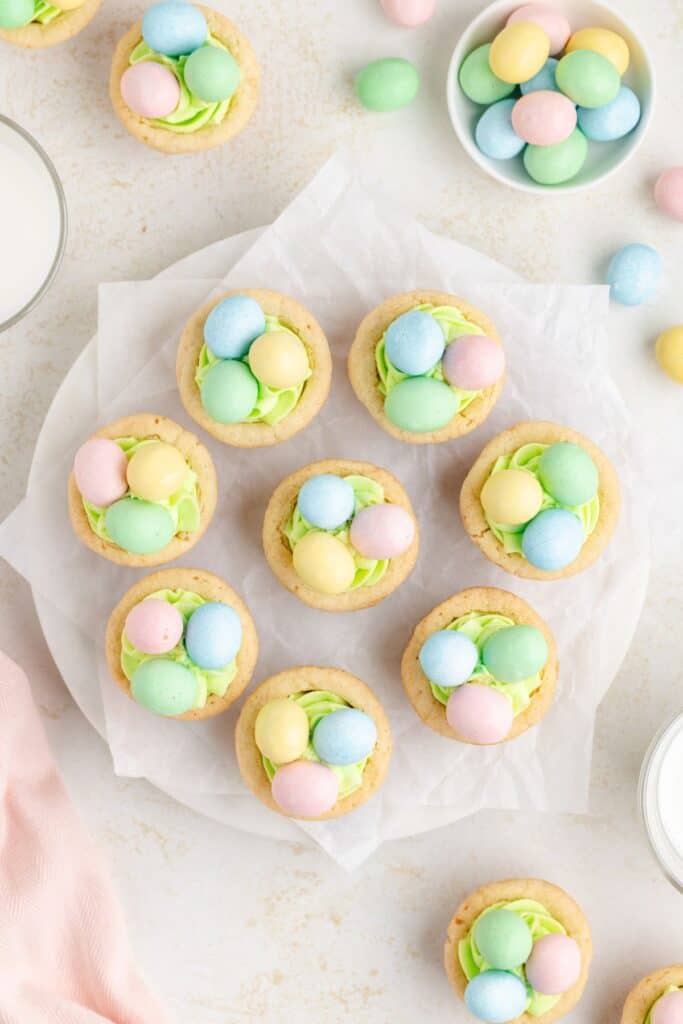 Cookie cups with pastel-colored Easter candy eggs on light green frosting, arranged on a round plate with parchment paper. 