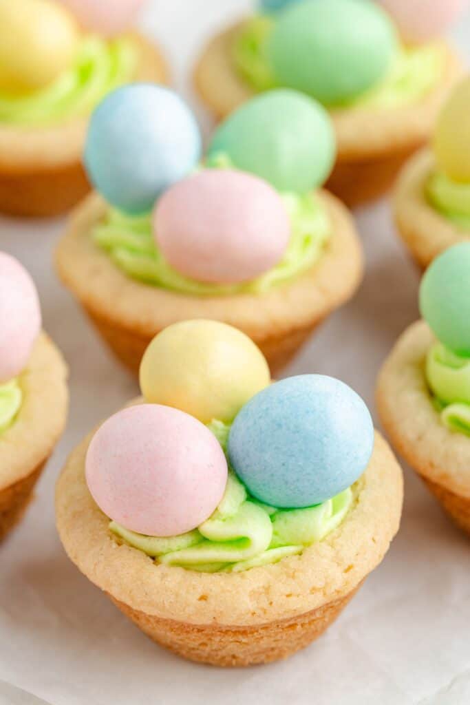 Easter cookie cups with green frosting, each topped with three pastel-colored candy eggs in pink, yellow, blue, and green.