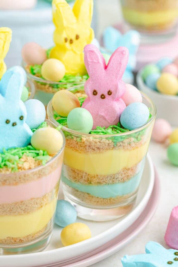 Colorful Eater dessert cups with layered pastel pudding, cookie crumbs, topped with marshmallow bunnies and candy eggs.