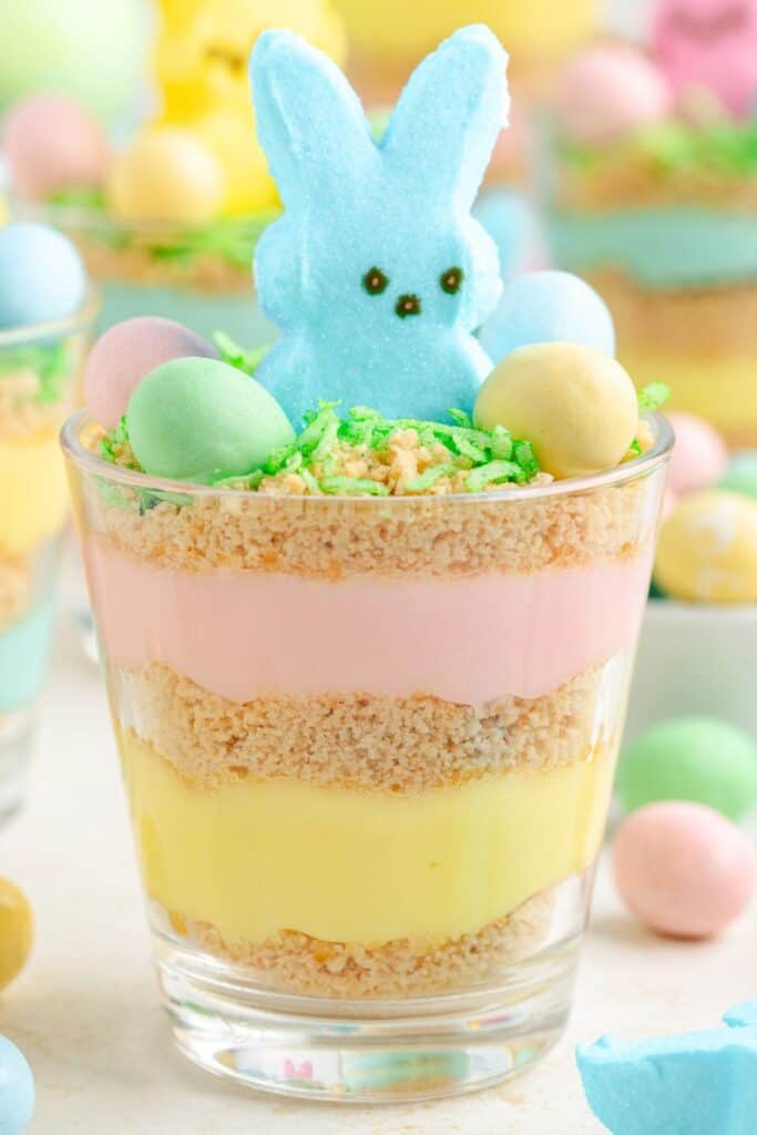 Layered pudding cup with pastel pudding, cookie crumbles, a blue marshmallow bunny, green coconut grass, and candy eggs.