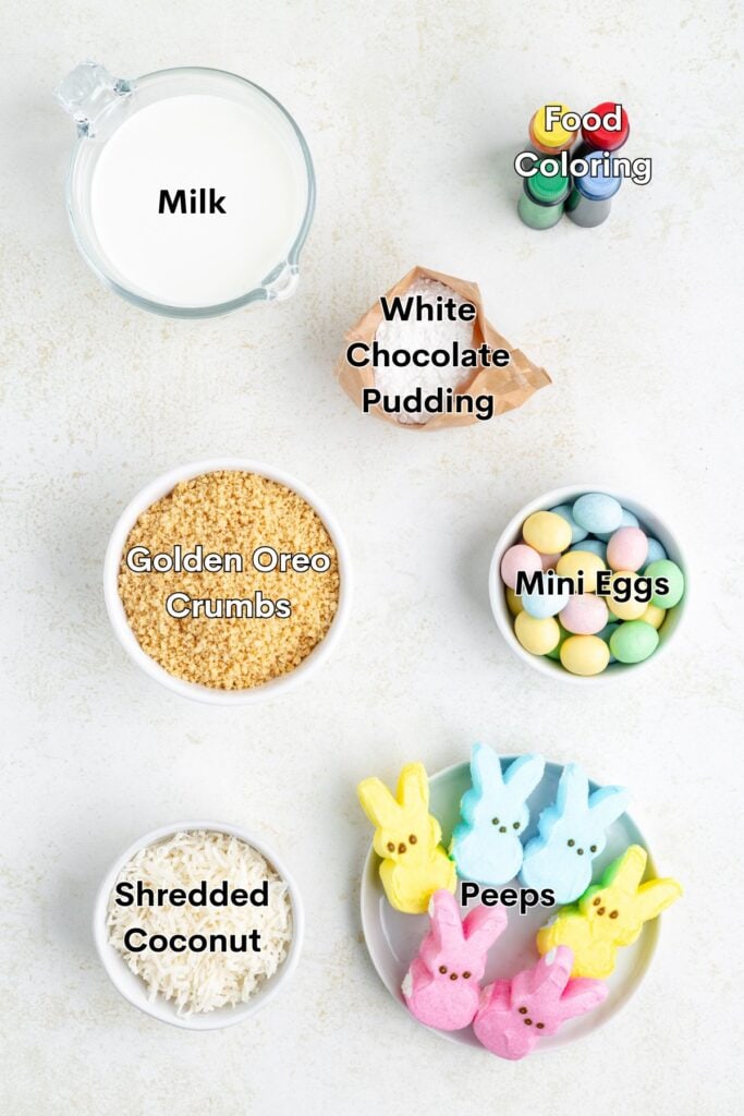 Assorted dessert ingredients: milk, food coloring, white chocolate pudding, mini eggs, crumbled Oreos, shredded coconut, and Peeps.