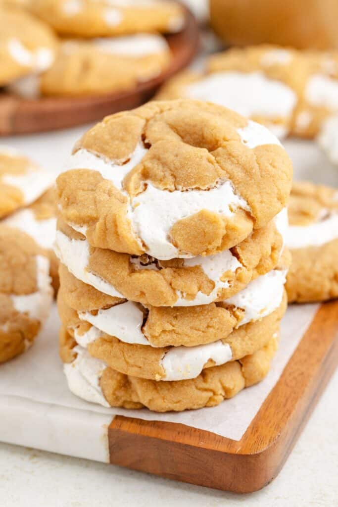 Stack of brown fluffernutter cookies with marshmallow swirls on a parchment-lined tray; others in the background.