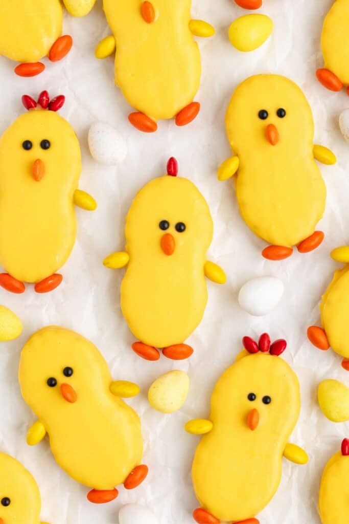 Chick-shaped Nutter Butter cookies with candy beaks and feet, surrounded by colorful candy eggs.
