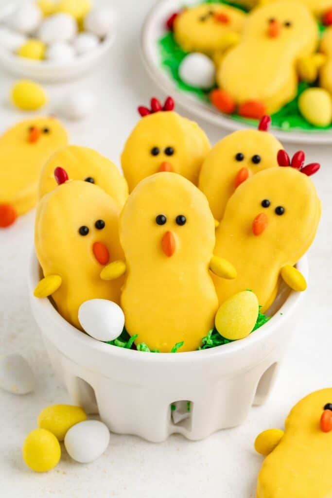 Nutter Butter chicks with candy eyes, orange beaks, and candy eggs in a white bowl.