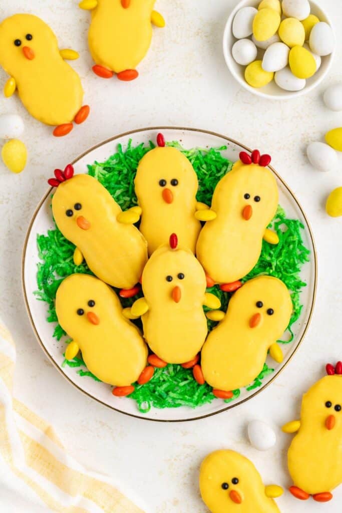 Yellow chick-shaped cookies with candy details on a plate with green coconut shreds.