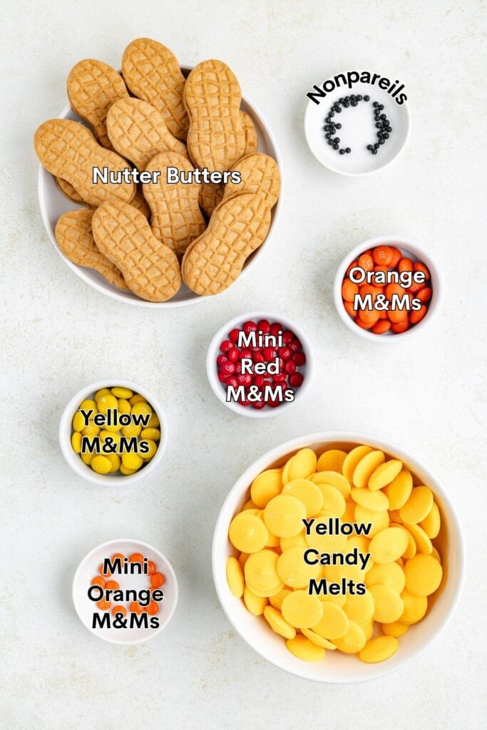 Assorted candies and cookies in bowls: Nutter Butters, nonpareils, various M&Ms, yellow candy melts.