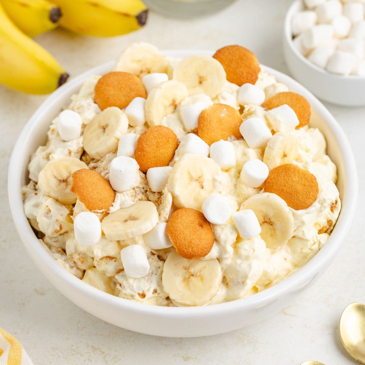 White bowl of creamy banana pudding fluff with banana slices, mini marshmallows, vanilla wafers.