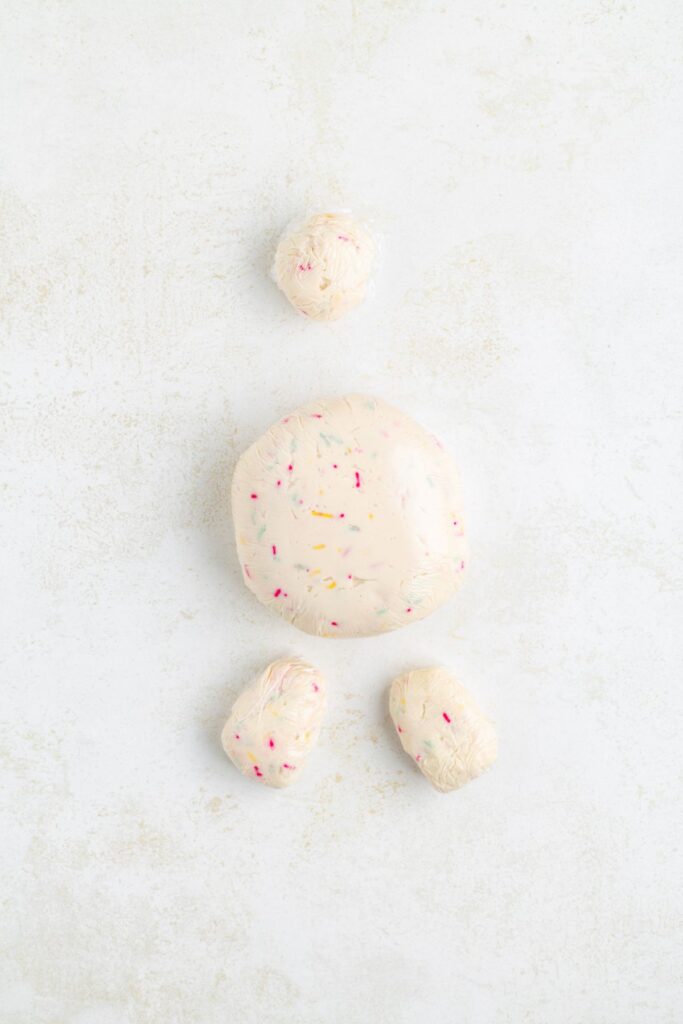 Round sweet cheese balls with colorful sprinkles wrapped in plastic on a white surface.