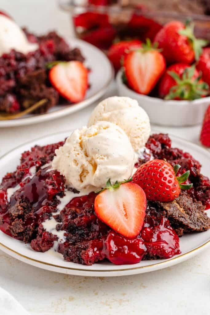 Chocolate strawberry dump cake topped with vanilla ice cream and fresh strawberries on a dessert plate.