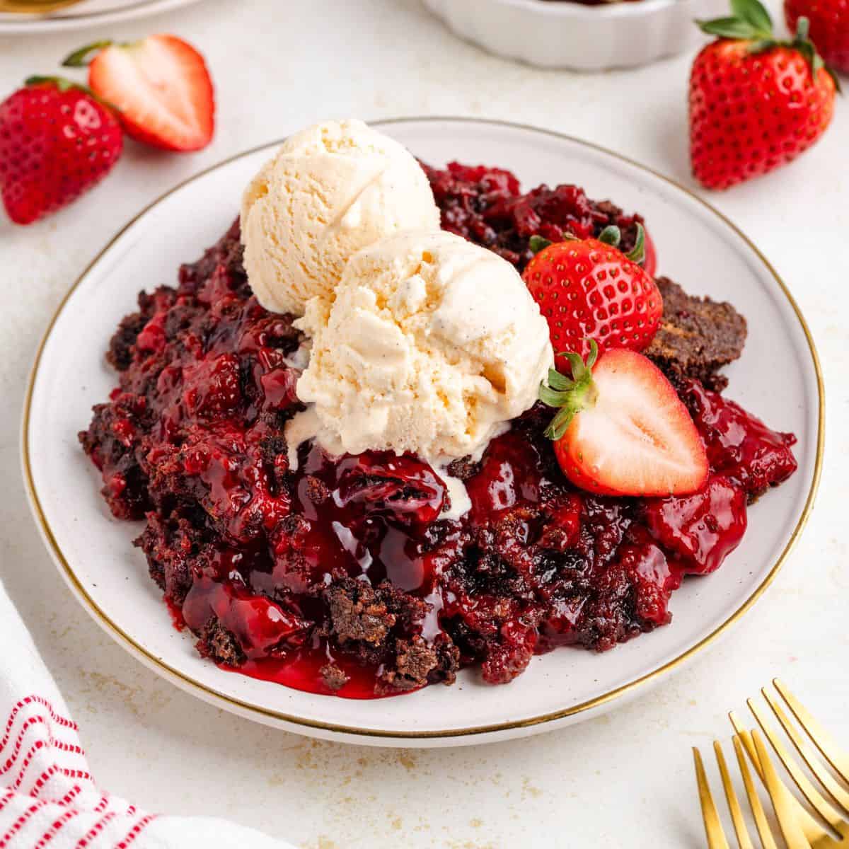 Chocolate strawberry dump cake with two vanilla ice cream scoops, garnished with fresh strawberries on a white plate.