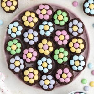 Mini brownies with colorful pastel M&Ms arranged as flower patterns on a pink plate.