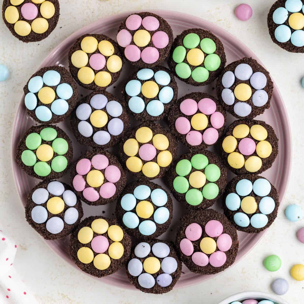 Mini brownies with colorful pastel M&Ms arranged as flower patterns on a pink plate.