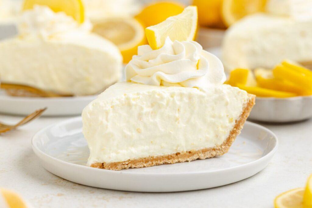 Slice of creamy Jello lemon pie with whipped cream and lemon wedge on a white plate.