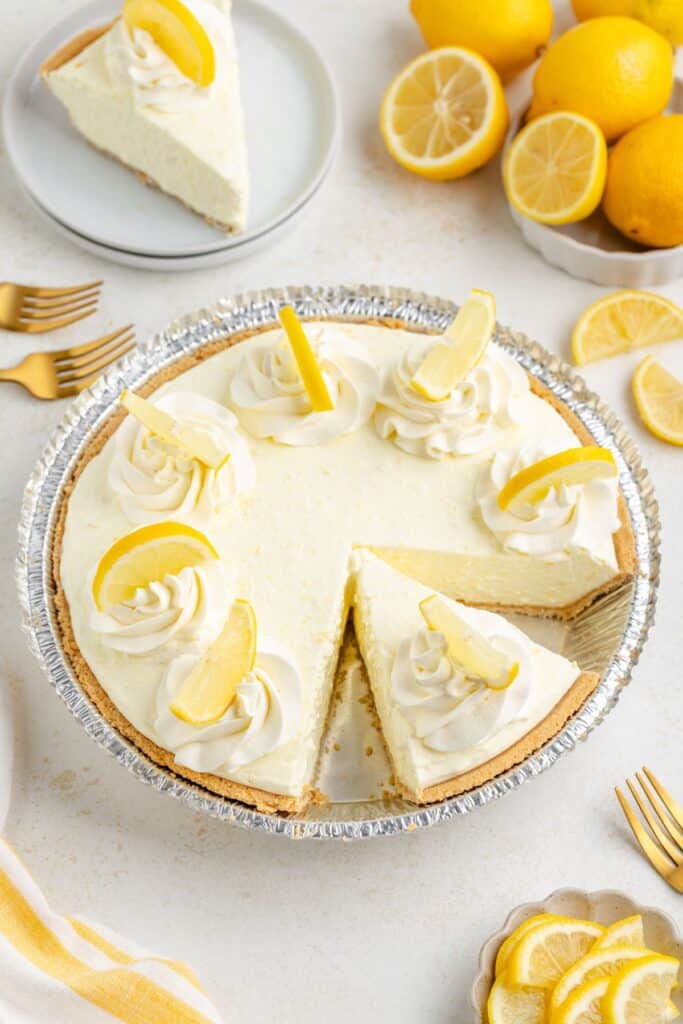 Lemon Jello pie with whipped cream, lemon slices, one slice missing; fresh lemons and gold forks around.