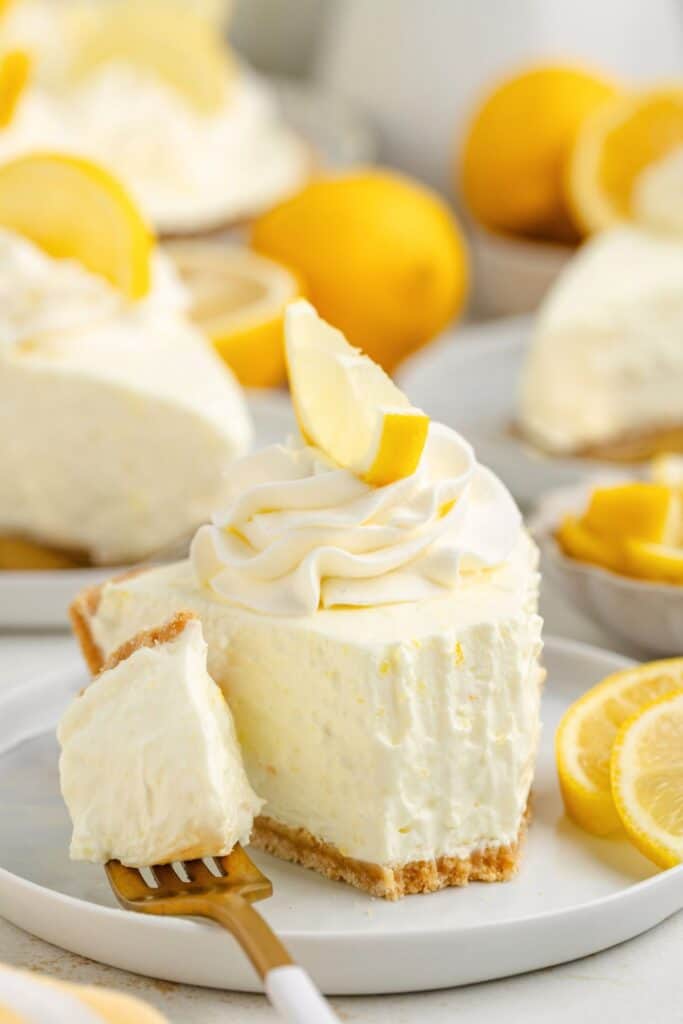 Slice of lemon Jello pie with whipped topping and wedge on plate; lemons and more pie in background.