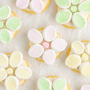 Cookies topped with pastel marshmallow flowers arranged on parchment paper.