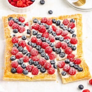 Berry puff pastry tart with cream, raspberries, blueberries, powdered sugar; cut into six pieces on puff pastry.