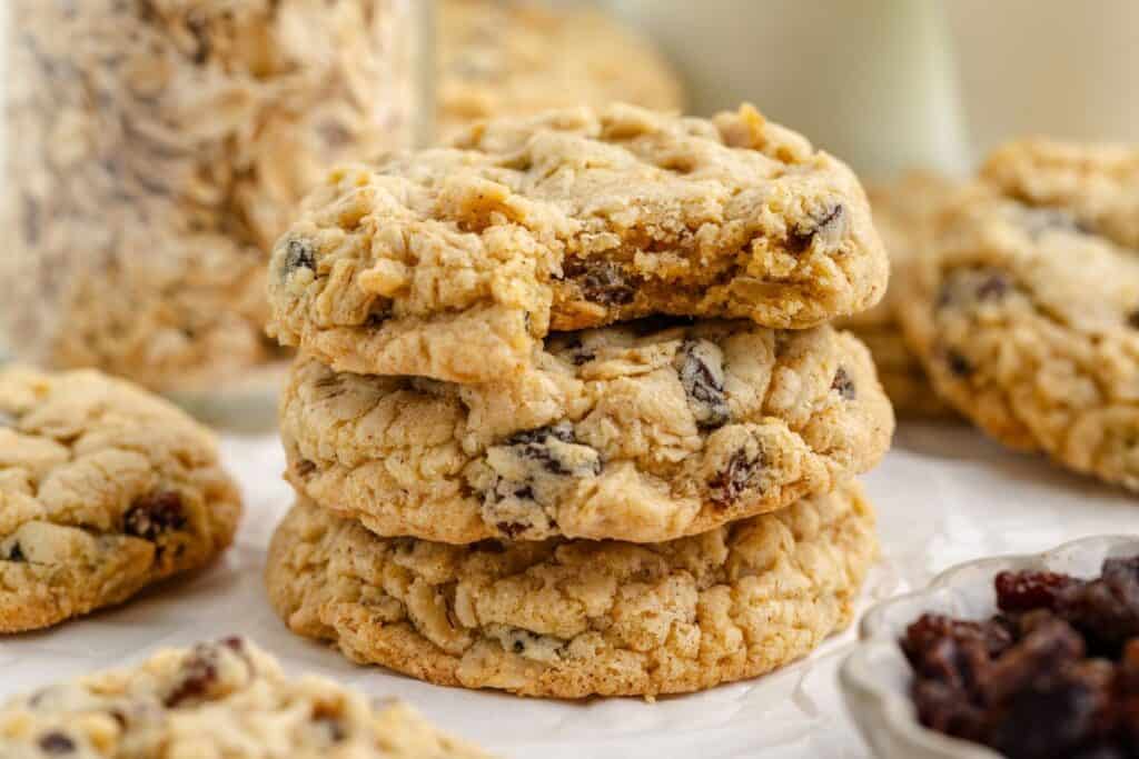 Stack of three oatmeal raisin cake mix cookies on parchment; more cookies and a bowl of raisins in background.