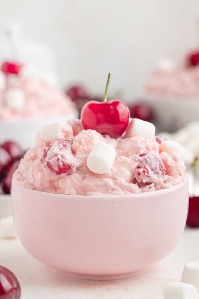 Cherry fluff dessert in a pink bowl, topped with a cherry and marshmallows.