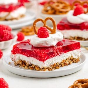 Slice of raspberry pretzel Jello salad topped with whipped cream, fresh raspberry, and pretzel on a white plate.