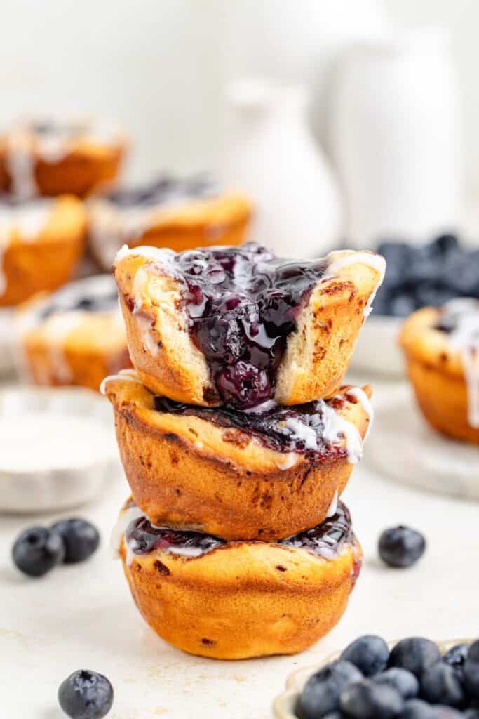 Stack of three blueberry muffin tin pies, top mini pie split revealing filling, surrounded by fresh blueberries.