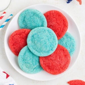White plate with four blue and three red cookies arranged in a circle on a light-colored surface.