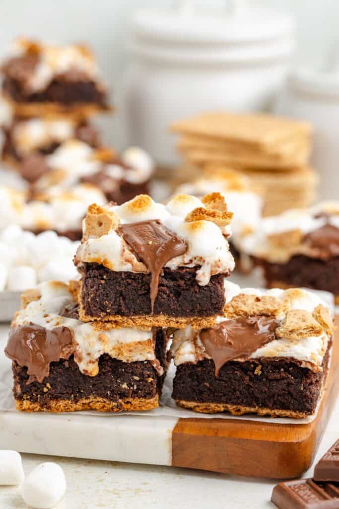 Three stacked smores brownies topped with toasted marshmallows and melted chocolate, surrounded by graham crackers and brownies.