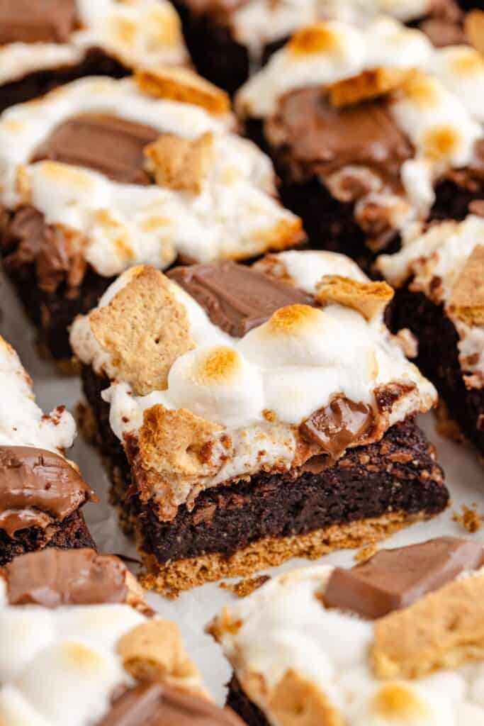 Close-up of brownies topped with toasted marshmallows, chocolate pieces, and graham cracker chunks on a tray.