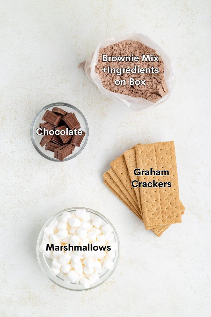 Four dessert ingredients—brownie mix, chocolate pieces, graham crackers, marshmallows—arranged and labeled on a white surface.
