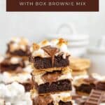 A stack of smores brownies topped with melted chocolate and marshmallows, surrounded by extra brownies and ingredients.