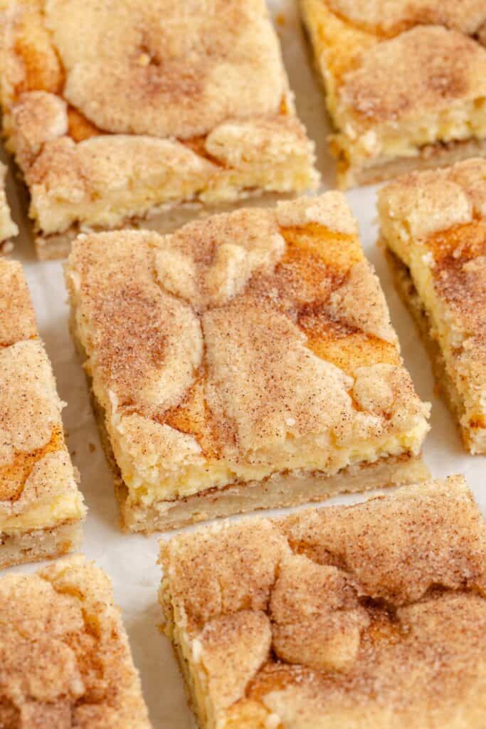 Close-up of Snickerdoodle cheesecake cookie bar with crumbly, layered texture, arranged on parchment paper.