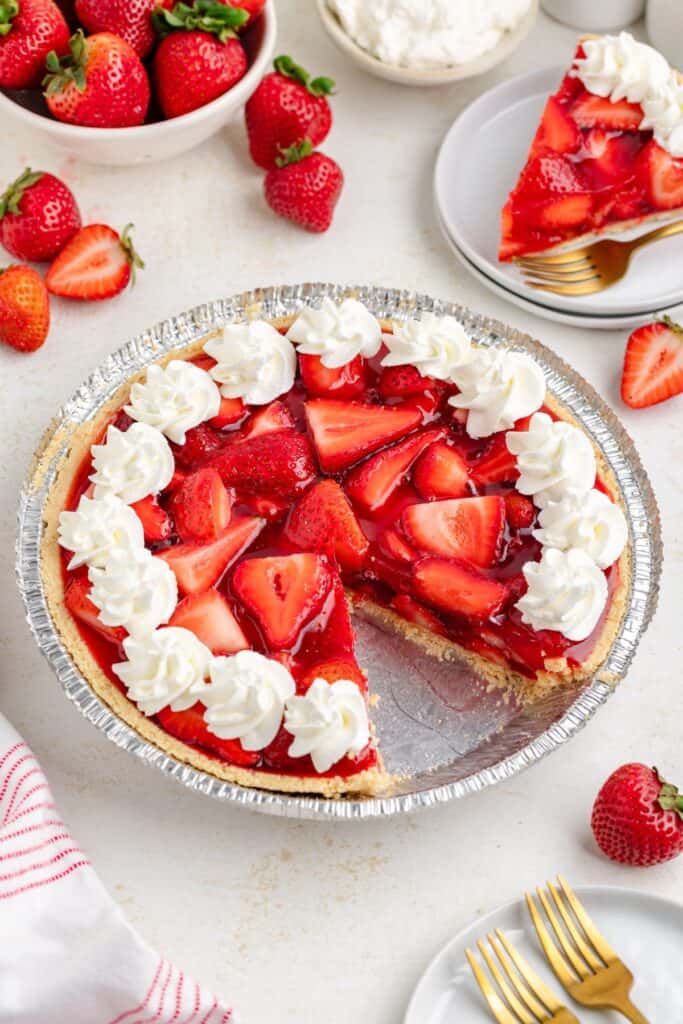 Strawberry pie with Jello, one slice on a plate, surrounded by fresh strawberries on the table.