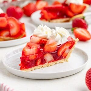 Slice of strawberry Jello pie with whipped cream on a white plate, showing fresh strawberry filling and flaky crust.