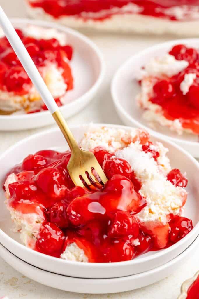 Close-up of a cherries in the snow on a dessert plate with fork; more slices visible behind.