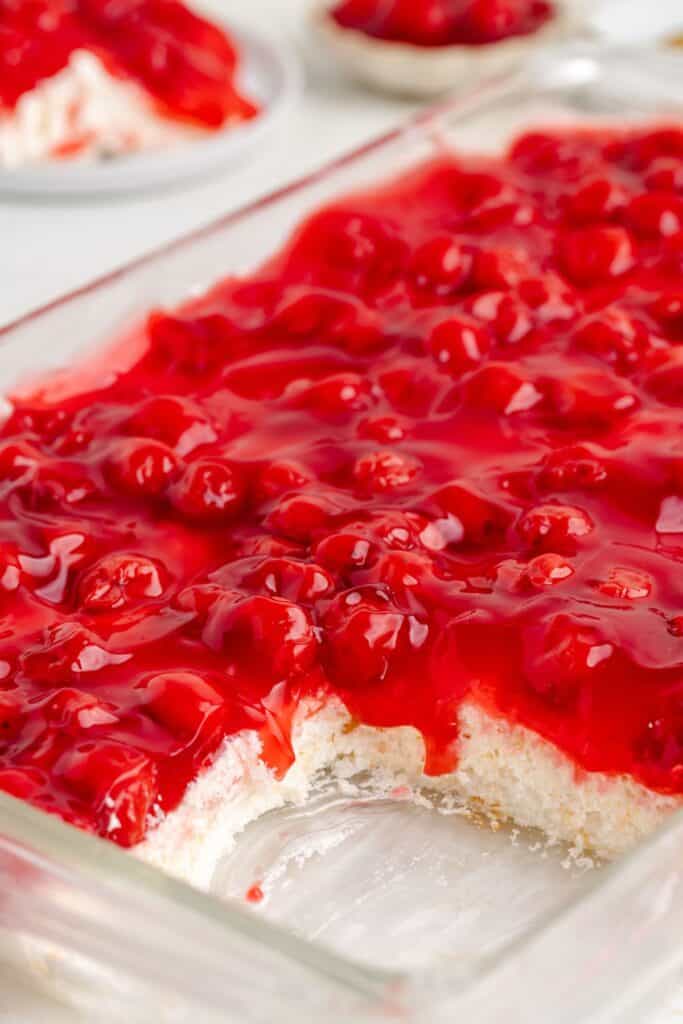 A glass dish of creamy dessert topped with cherry pie filling, with one serving removed.