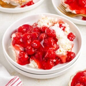 Cherries in the snow dessert on a white plate, with extra plates and forks blurred in the background.