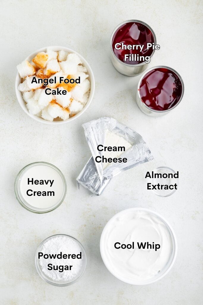 Seven labeled dessert ingredients—cake, cherries, cream cheese, extract, whipped topping, powdered sugar, cream—on white surface.