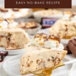 Slice of No Bake Snickers Pie topped with whipped cream and Snickers pieces, plated with fork; more slices behind.