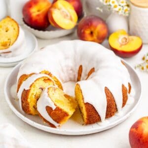 Sliced each bundt cake with vanilla glaze, surrounded by fresh peaches and white flowers on a light background.
