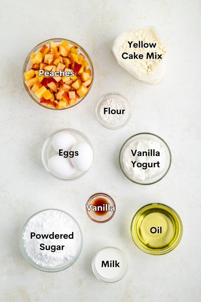 Top-down view of labeled bowls containing ingredients for peach cake, arranged neatly on a white background.