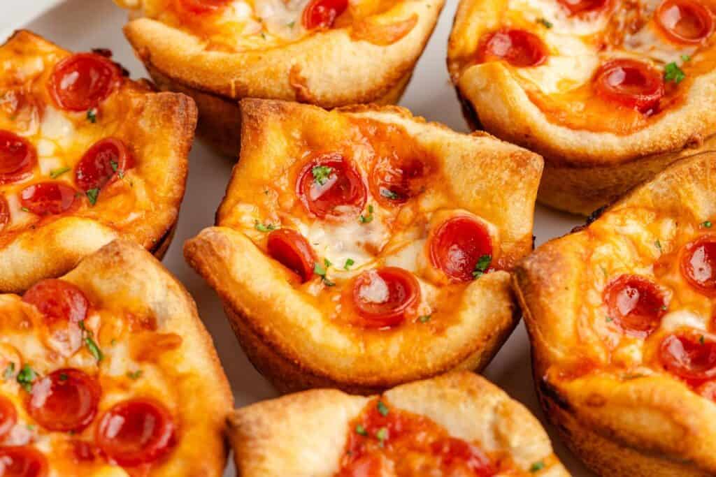 Mini pepperoni pizza cups with golden crust, melted cheese, and pepperoni slices grouped on a white surface.