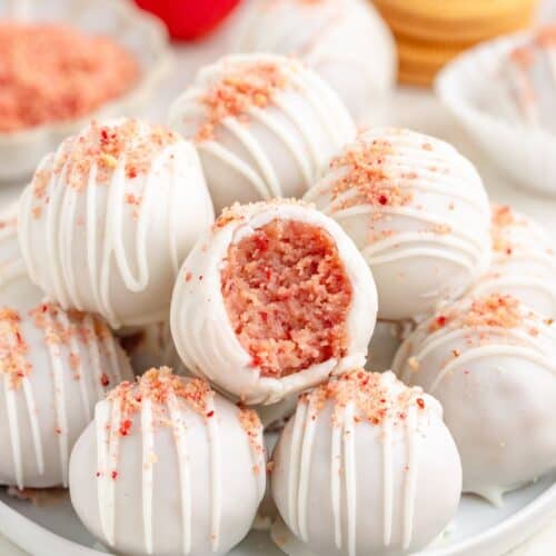 Strawberry shortcake truffles with pink filling, drizzled and sprinkled, one truffle showing the crumbly pink inside.