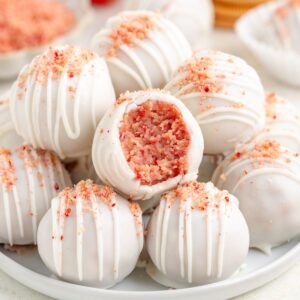 Plate of strawberry shortcake truffles with pink crumbs; one bitten to reveal pink interior.