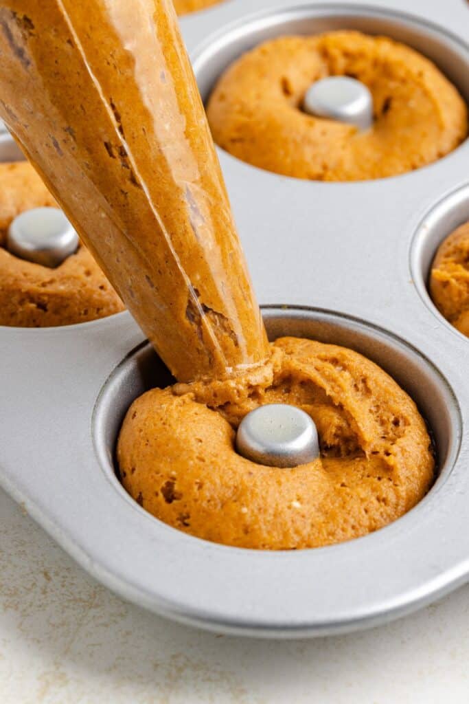 Pumpkin batter is piped from a bag into a metal donut pan.