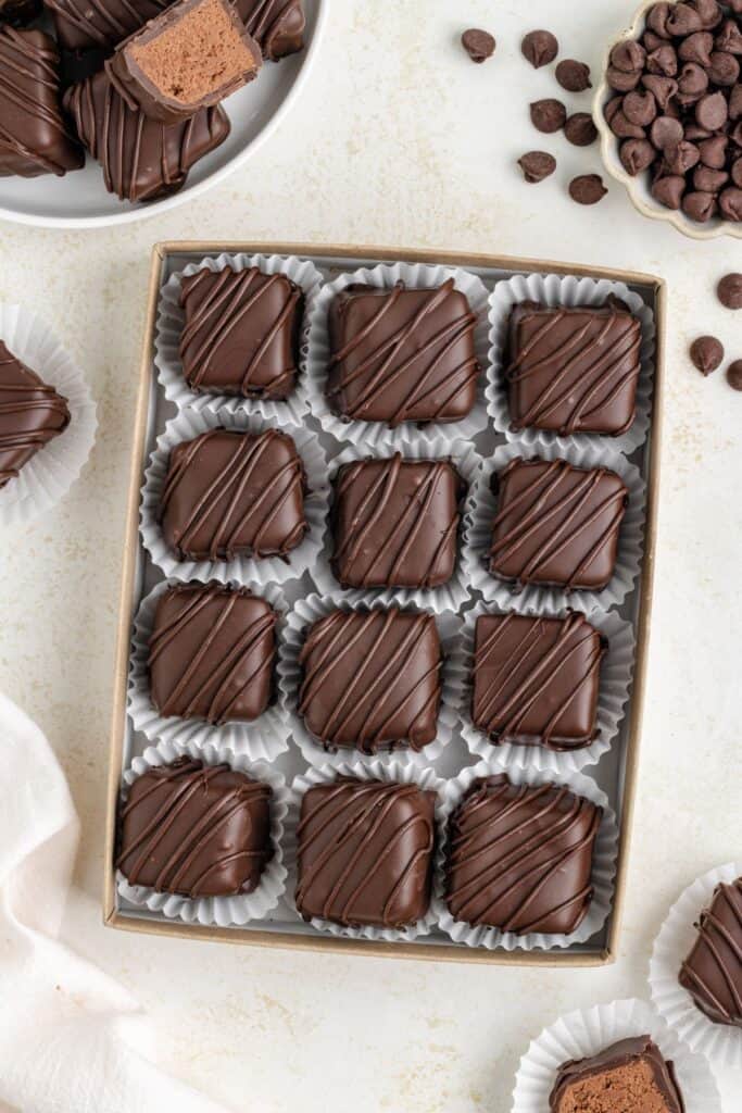 A box of twelve homemade 3 Musketeers candies with drizzled lines, alongside a bowl of chocolates and chocolate chips.