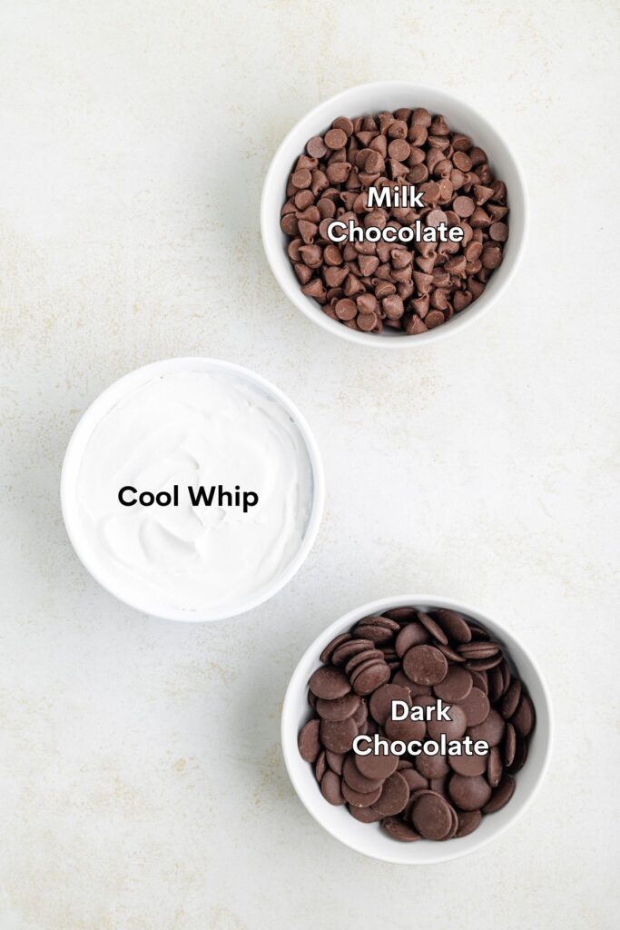 Three labeled bowls on a white surface hold milk chocolate chips, Cool Whip, and dark chocolate wafers.