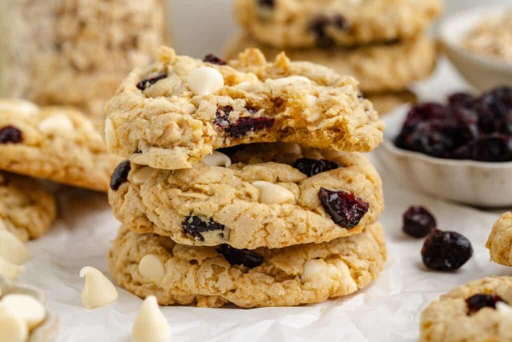 Stack of three oatmeal cranberry white chocolate cookie, surrounded by more cookies on parchment.