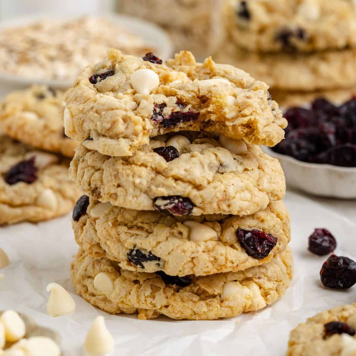Stack of oatmeal cranberry white chocolate cookies, surrounded by extra cookies and scattered ingredients.